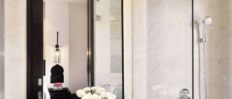 Un baño moderno con un espejo grande, un lavabo, una ducha con cerramiento de vidrio y un florero con flores.