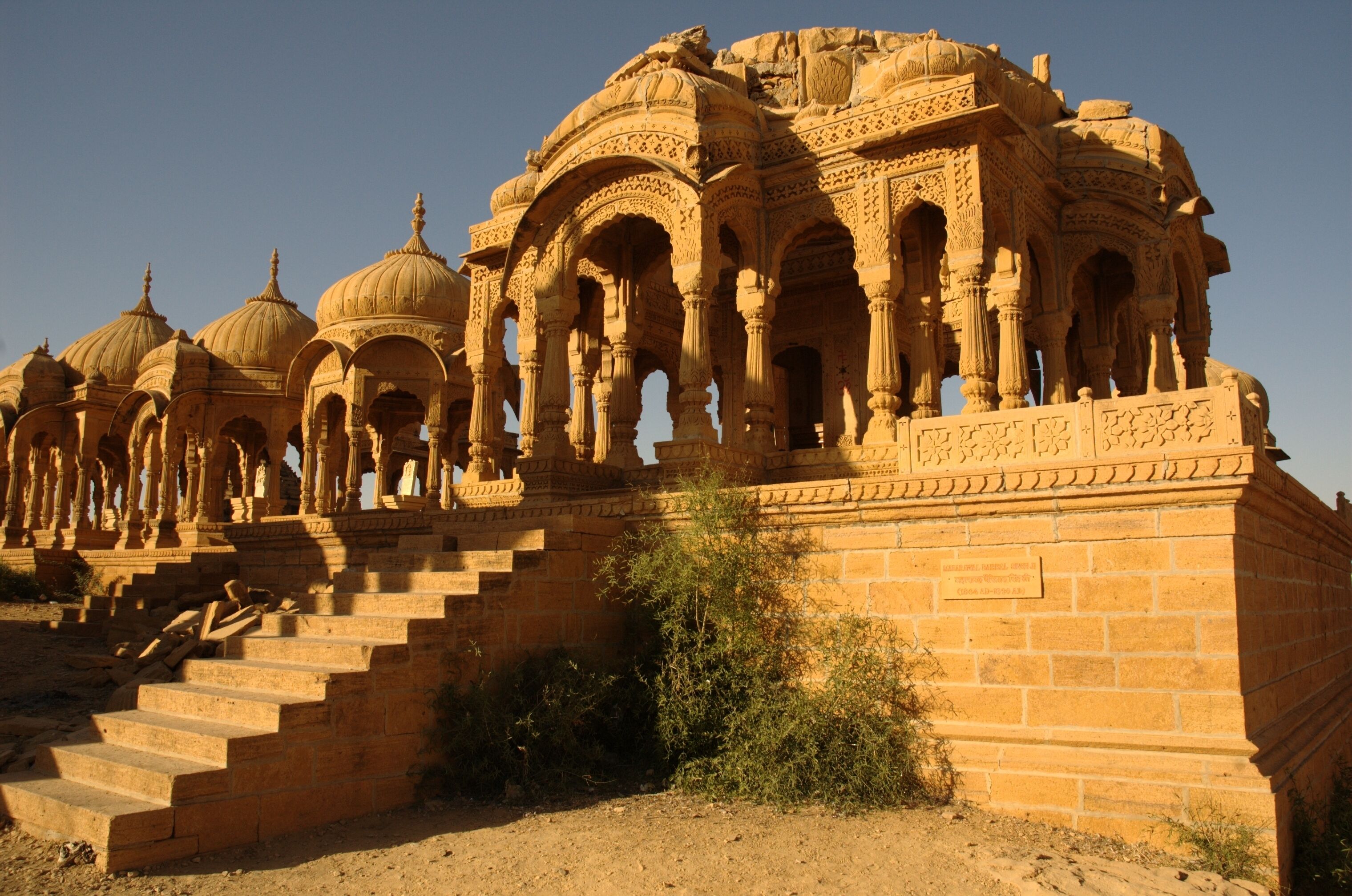 A historic building with multiple domes and arches, featuring intricate carvings and a stone staircase leading up to the entrance.