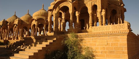A historic building with multiple domes and arches, featuring intricate carvings and a stone staircase leading up to the entrance.