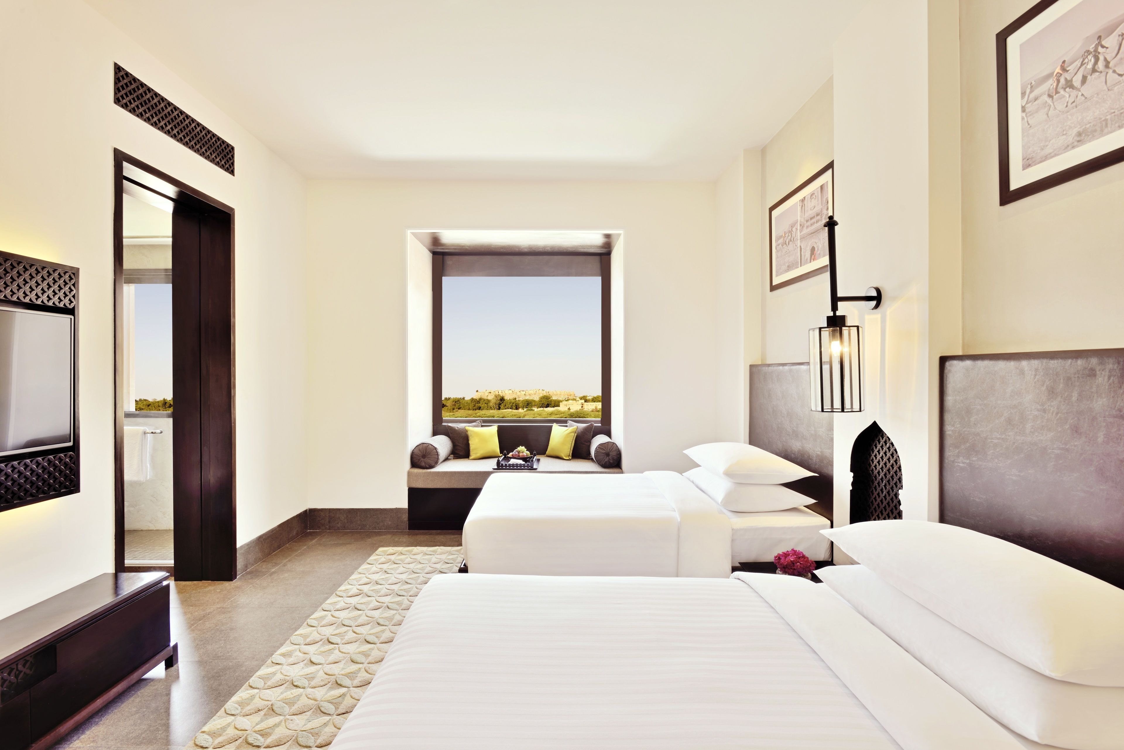 A hotel room with a large bed, a smaller bed, a TV, a window with a view, and a bathroom visible through an open door.