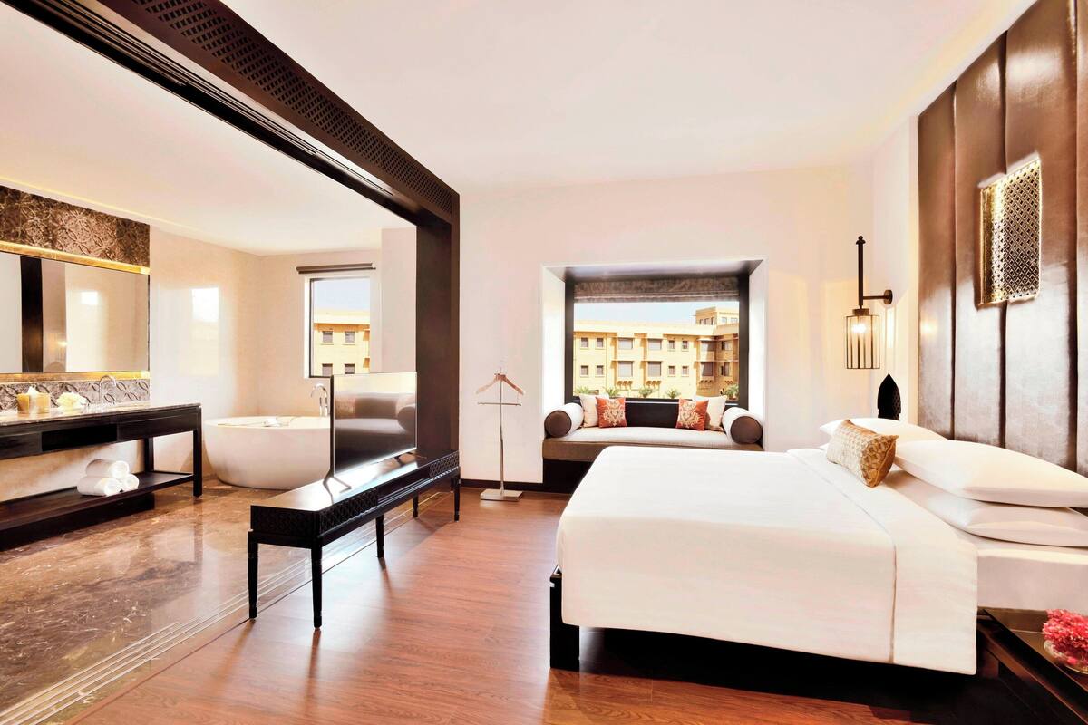 Ein modernes Hotelzimmer mit einem großen Bett, einer Badewanne, einem Schminktisch mit Spiegel und Blick auf die Stadtlandschaft.