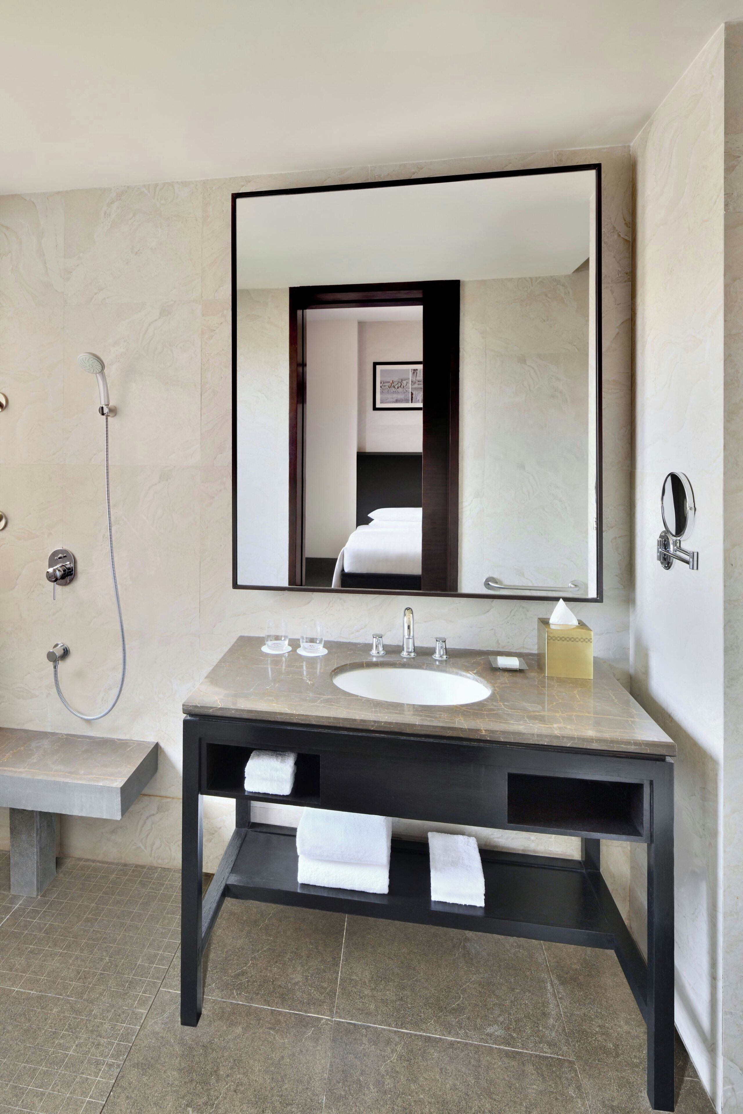A modern bathroom with a marble vanity, a large mirror, a handheld showerhead, and a towel rack.