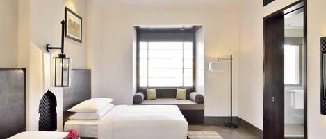 Habitación de hotel con dos camas, un ventanal grande, una zona de estar con un banco y un espejo en la pared.