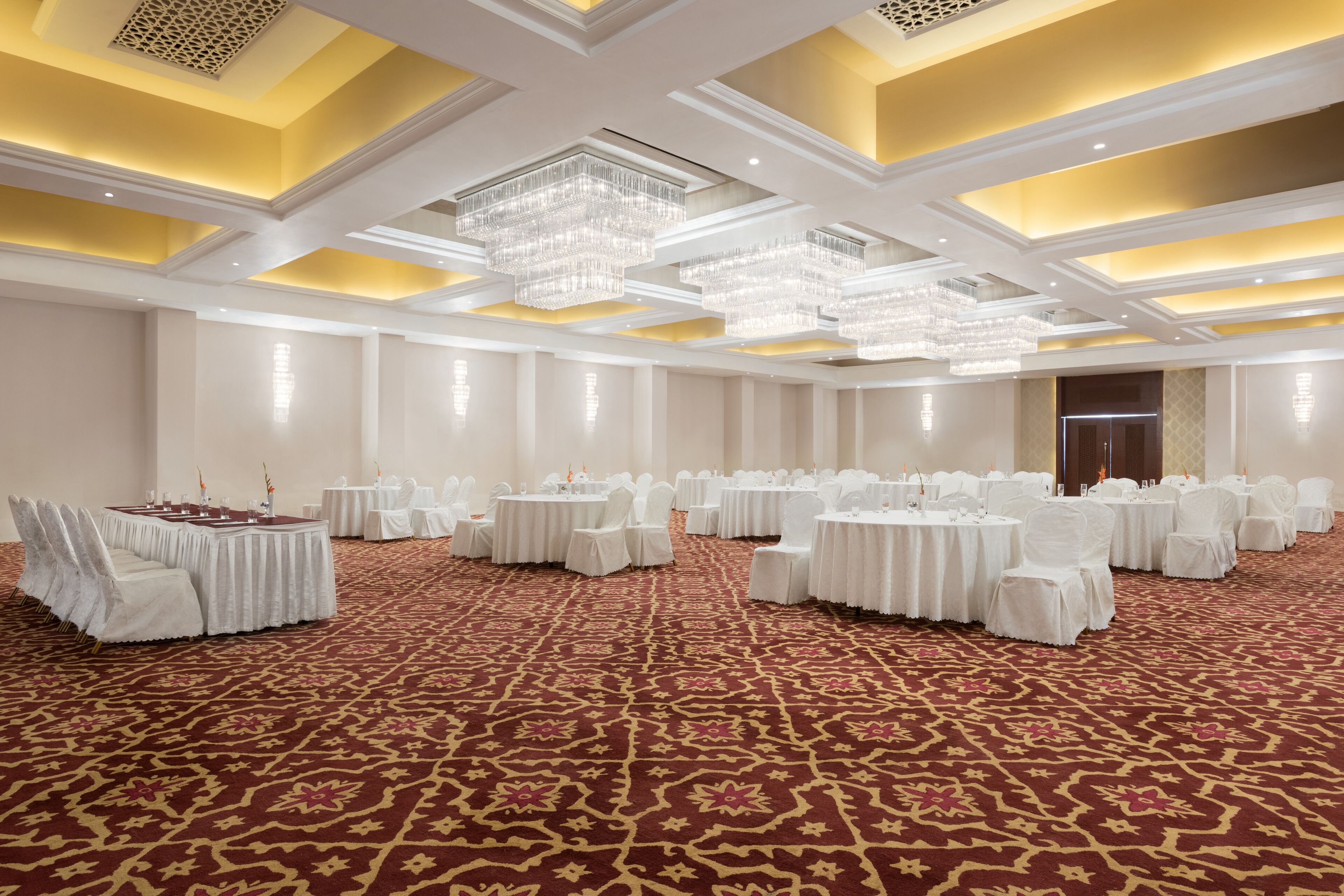 Une vaste salle de banquet avec de nombreuses tables rondes, des chaises blanches et des lustres.