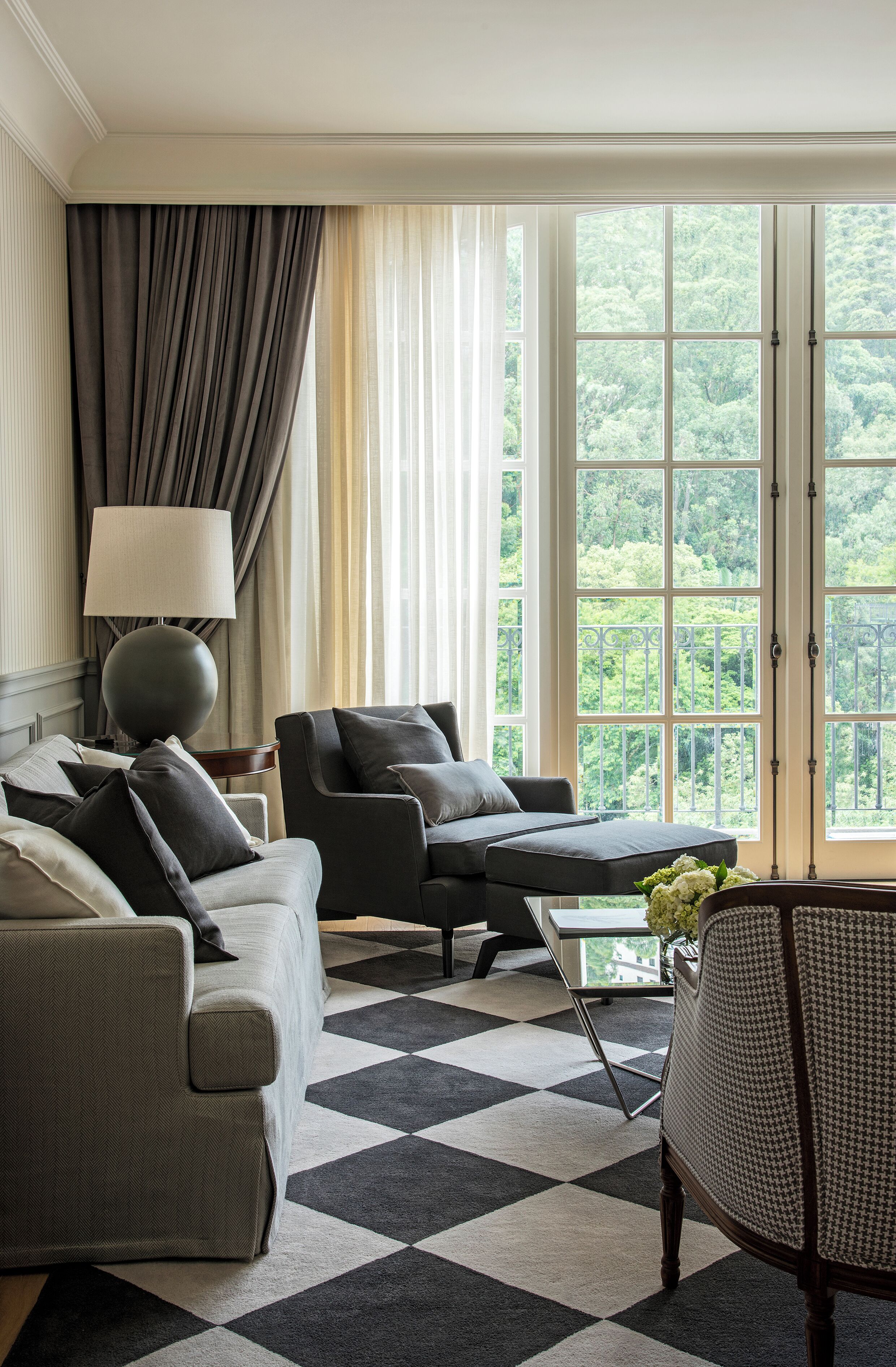 A modern living room with a checkered carpet, a sofa set, a coffee table, and a view of lush greenery through large windows.