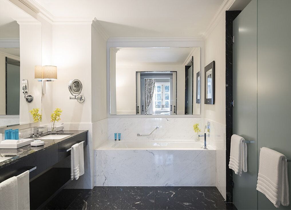 A modern bathroom with a large bathtub, a double sink vanity, and a mirror with a wall-mounted lamp.
