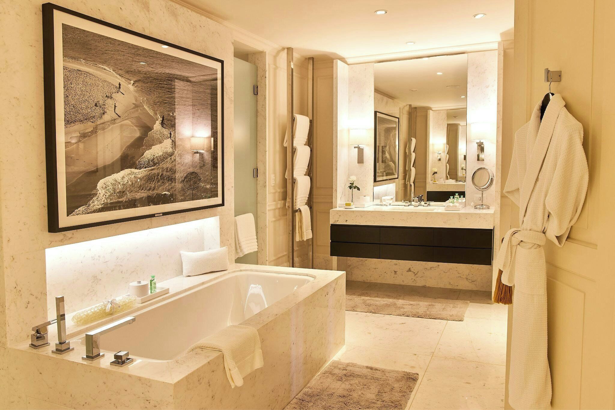 A modern bathroom with a large bathtub, a double sink vanity, and a framed artwork on the wall.