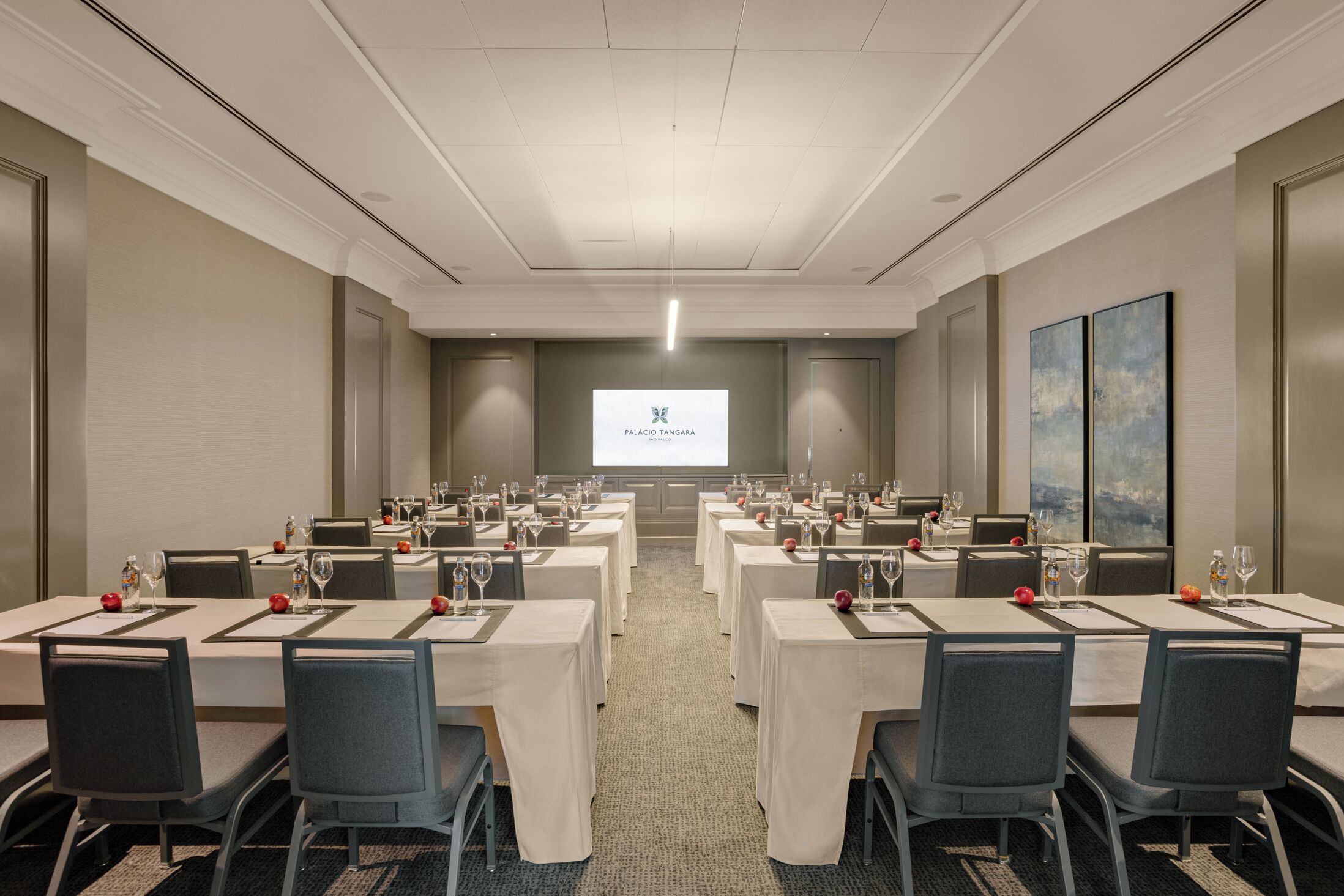 A conference room with tables set for a meeting, a projector screen displaying a logo, and a large abstract painting on the wall.