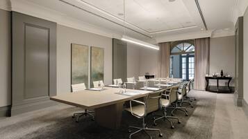 A conference room with a long table, chairs, and a small table with a laptop.