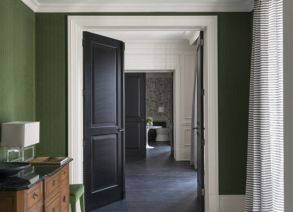 Um corredor com portas de madeira escura, parede verde e cortina listrada.