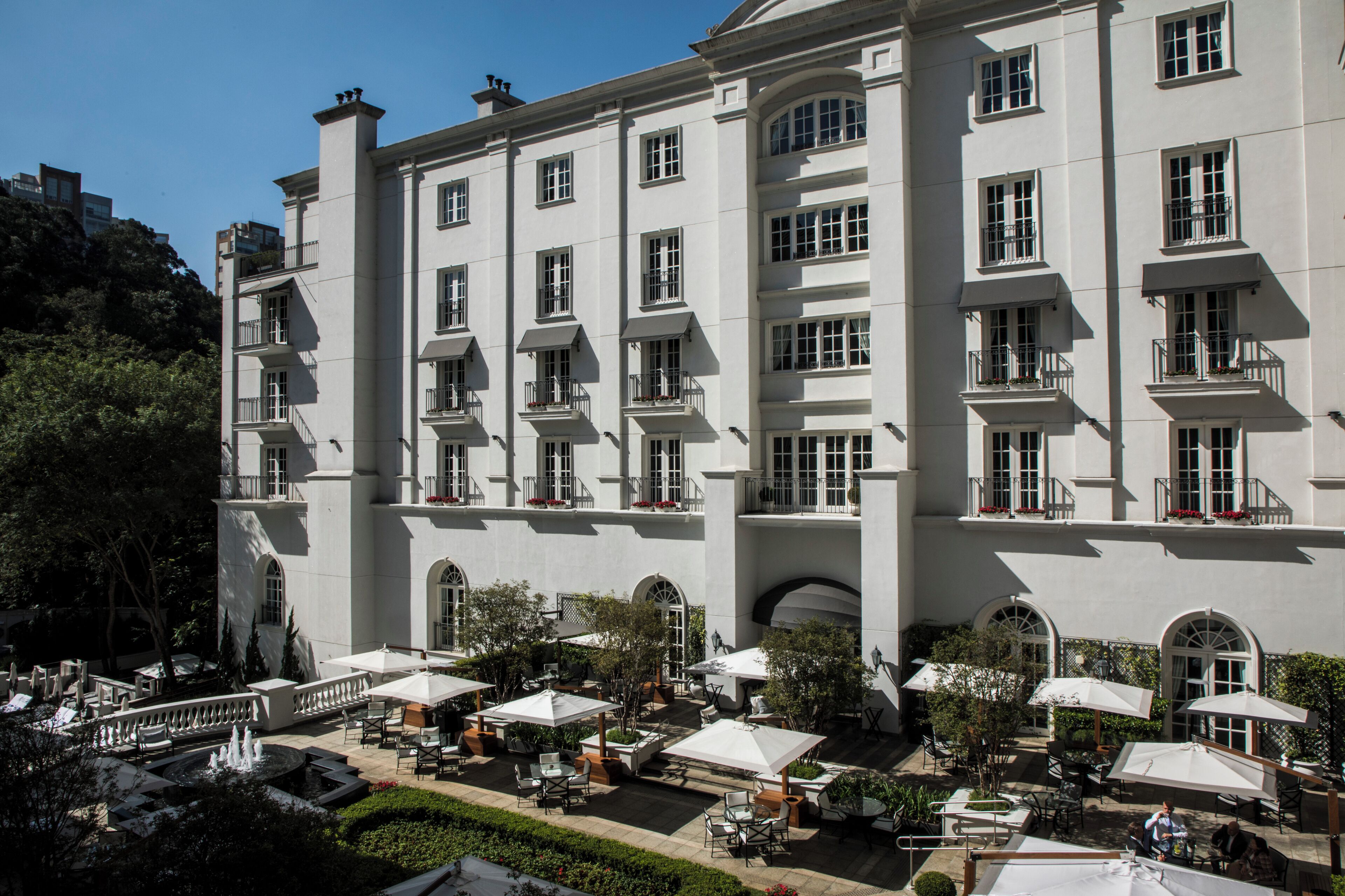 A large, multi-story building with balconies, outdoor seating areas, and a fountain.