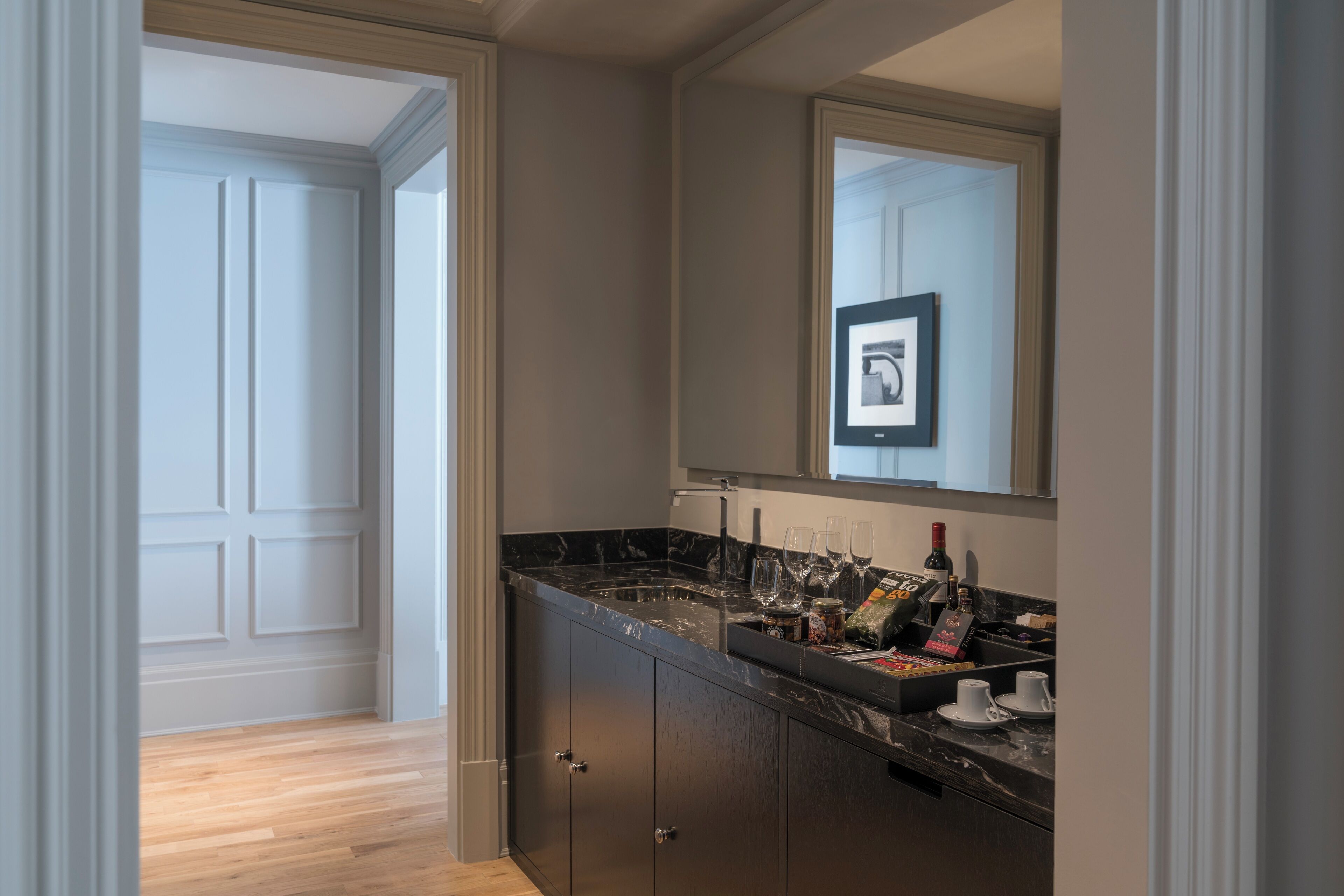 Un bagno moderno con un piano d'appoggio in marmo scuro, uno specchio grande e un quadro incorniciato sopra lo specchio.