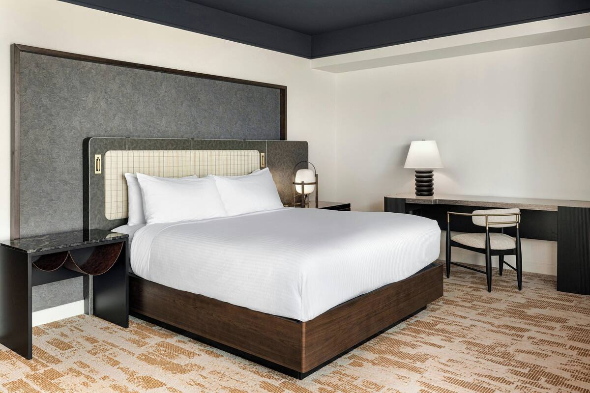 Una habitación de hotel con una cama grande, un escritorio, una silla y una mesita de noche.