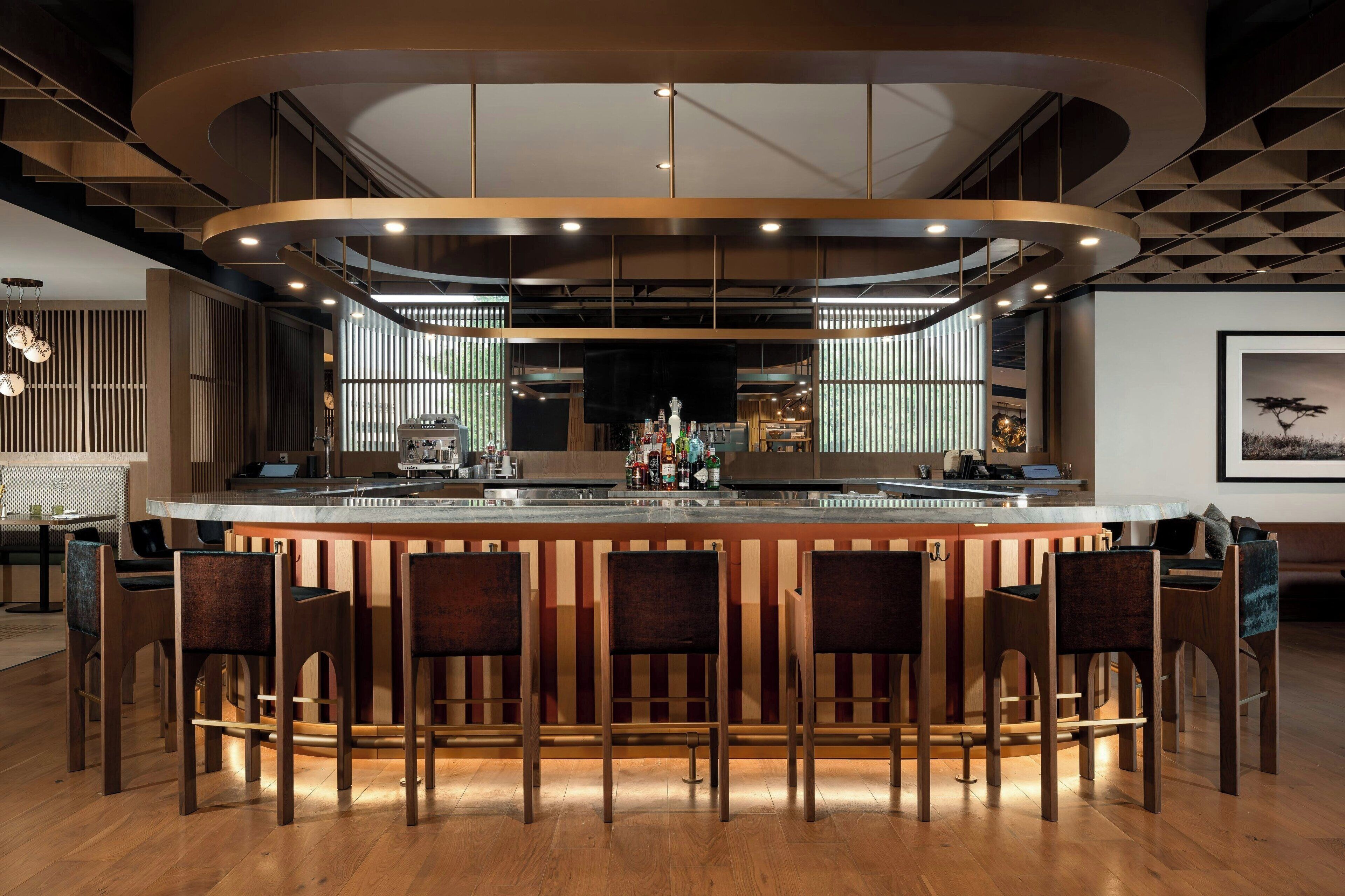 Een moderne bar met een gebogen toonbank, meerdere barkrukken en een groot scherm.