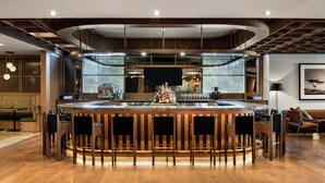 A modern bar area with a curved counter, bar stools, and a central television screen. - The Elmore Hotel, DFW Southlake, a Tribute Portfolio Hotel (Southlake)