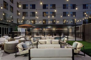 A rooftop patio with outdoor seating, string lights, and a view of a building in the background. - The Elmore Hotel, DFW Southlake, a Tribute Portfolio Hotel (Southlake)