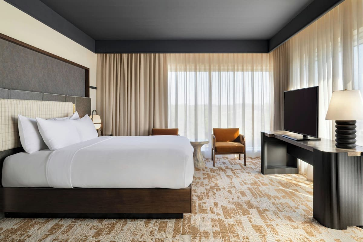 Una habitación de hotel con una cama grande, un escritorio, una silla, un televisor y una lámpara.