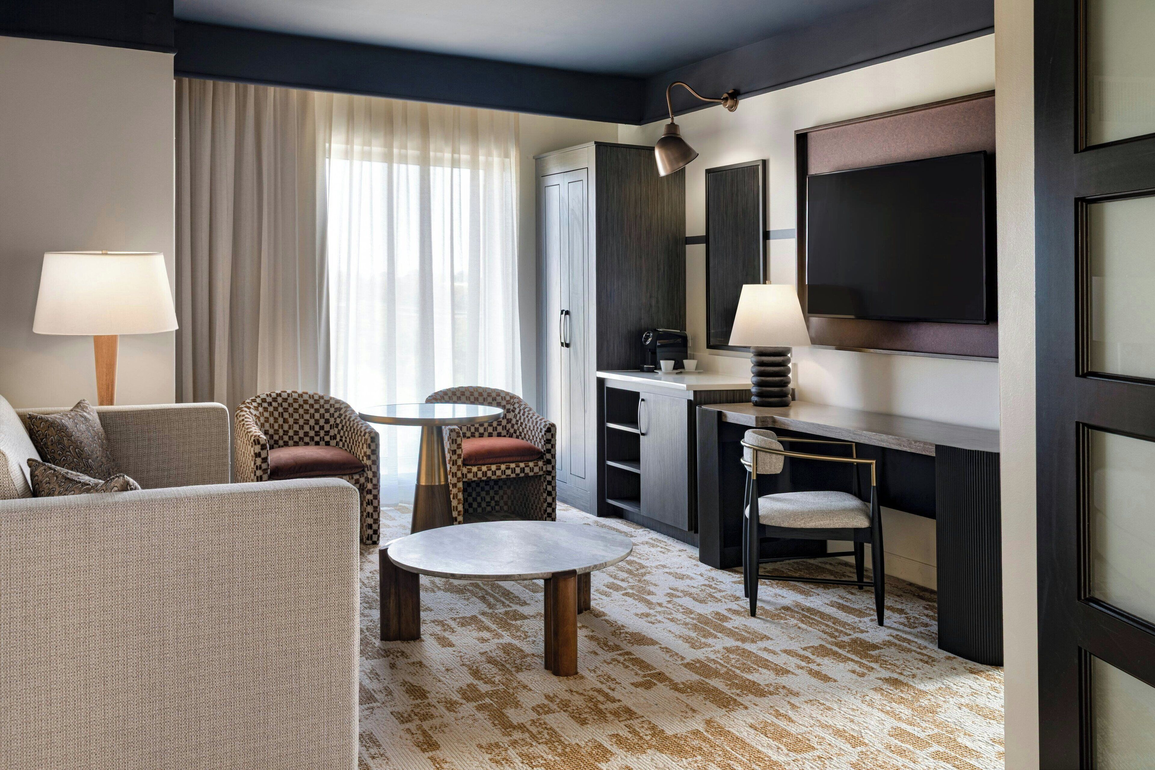 A modern hotel room with a living area, a dining table, a sofa, and a TV.