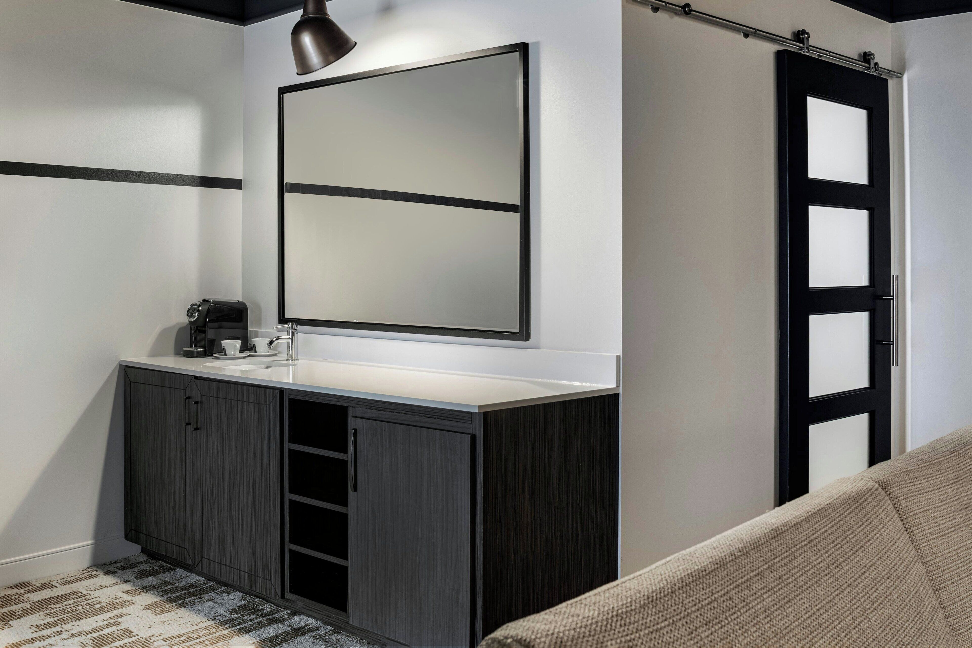 A modern bathroom with a dark wood vanity, a large mirror, and a black door with frosted glass panels.