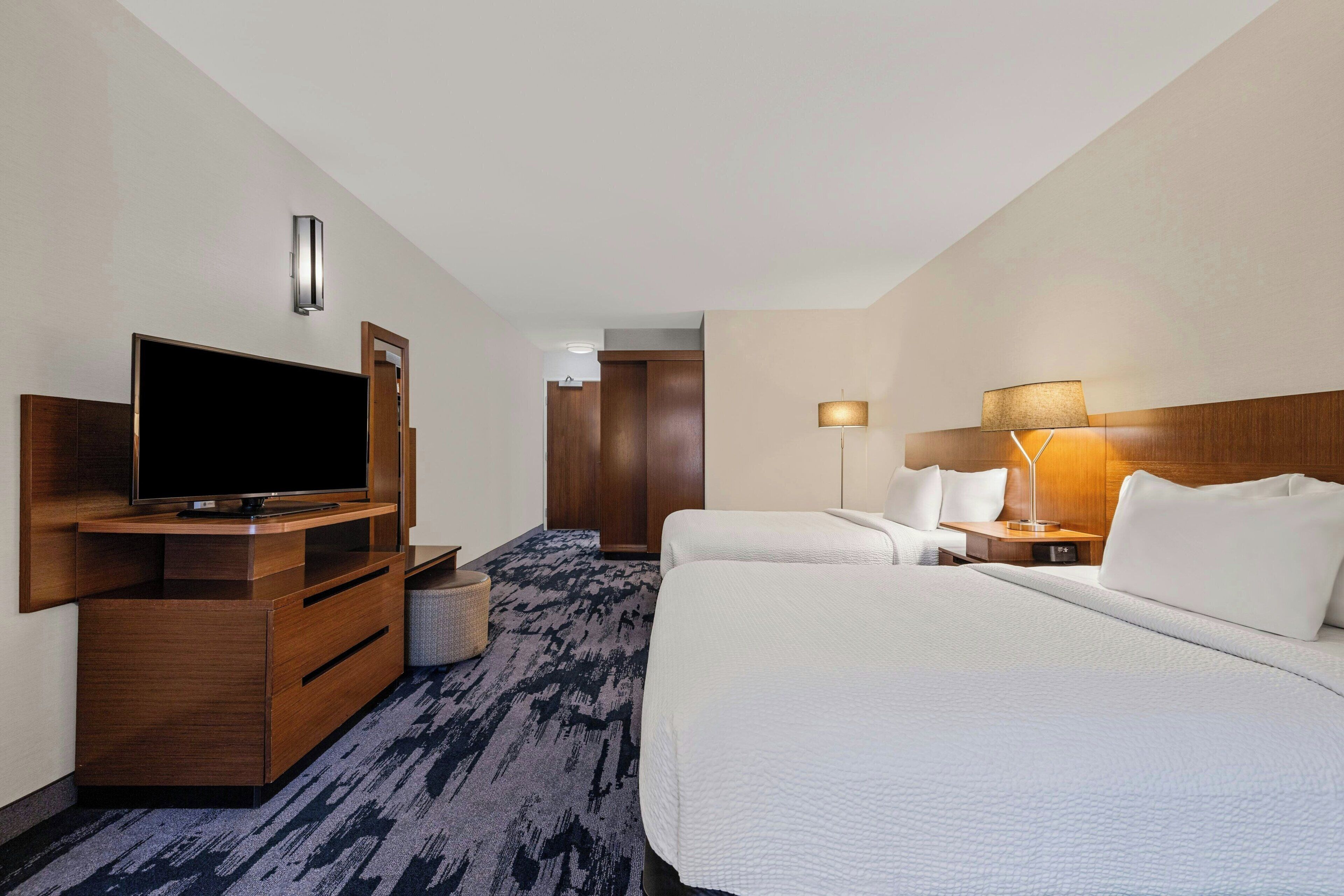 Ein Hotelzimmer mit einem großen Bett, einem Fernseher, einem Schreibtisch und einer Lampe.