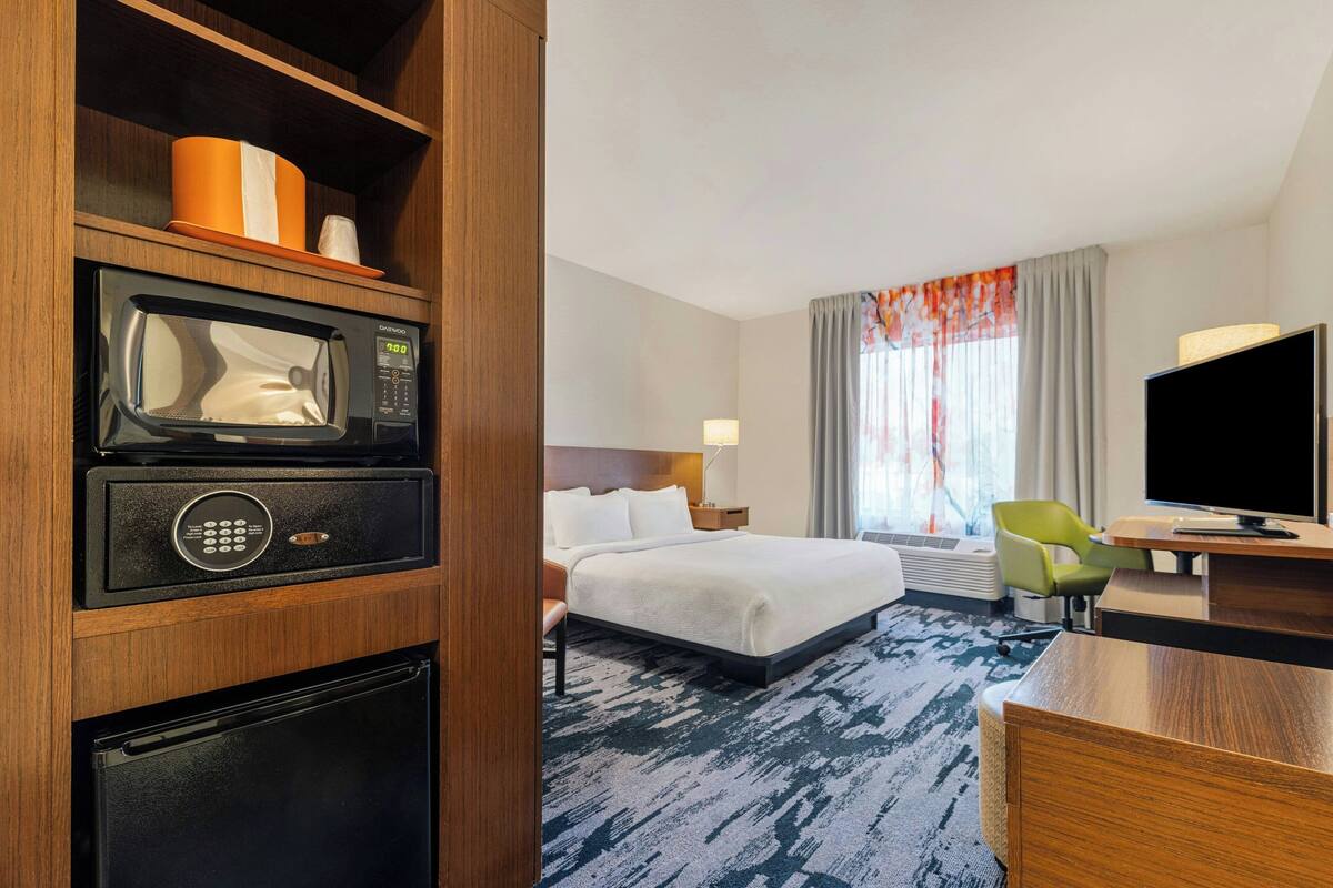 A hotel room with a bed, a desk, a television, a microwave, and a refrigerator.