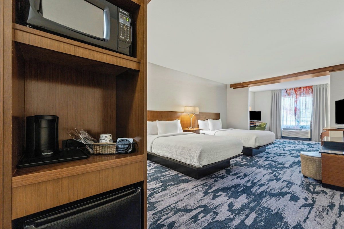 A hotel room with a bed, a desk, a microwave, and a minibar.