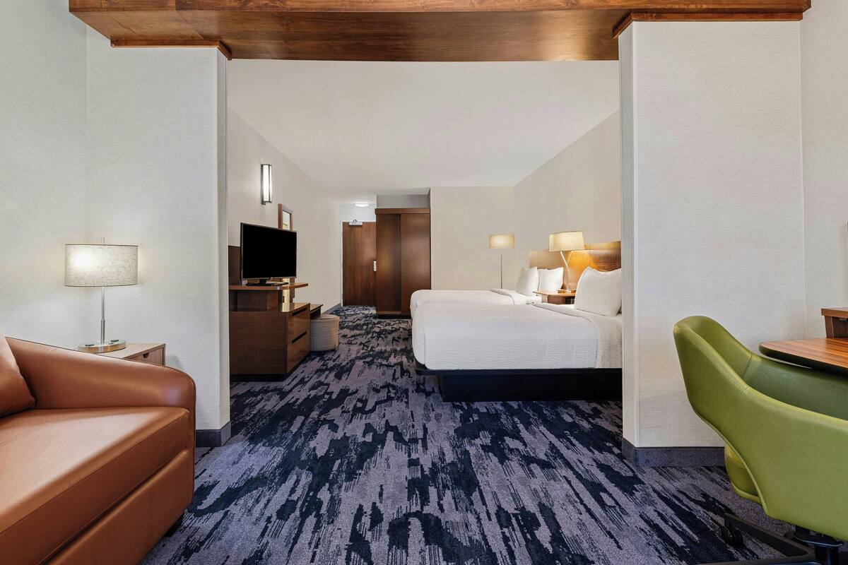 A hotel room with a bed, a green chair, a desk, a TV, and a lamp.