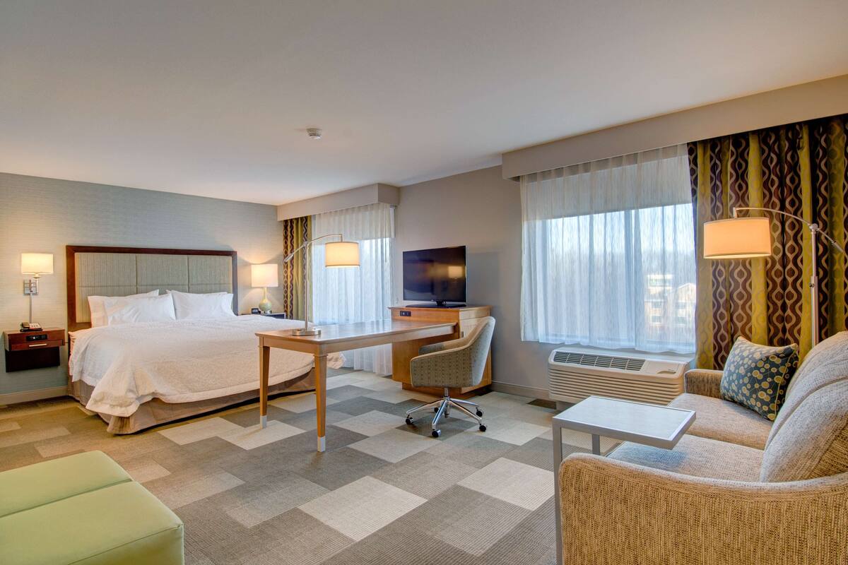 A hotel room with a bed, desk, chair, sofa, and TV.