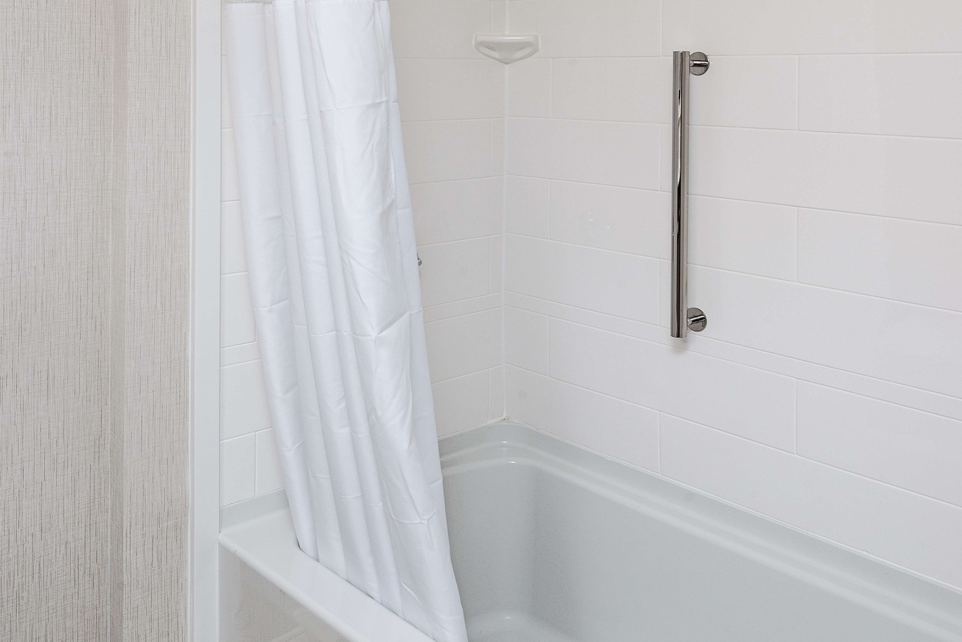 A bathroom with white tiled walls, a white bathtub, and a shower curtain.