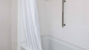 A bathroom with white tiled walls, a white bathtub, and a shower curtain.
