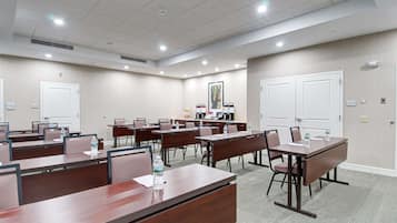 A conference room with multiple tables and chairs, equipped with water bottles and papers, and a coffee station in the background.
