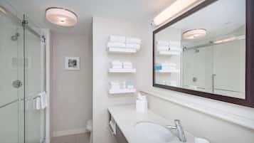 Un bagno moderno con box doccia in vetro, uno specchio grande e asciugamani ordinatamente disposti su mensole.