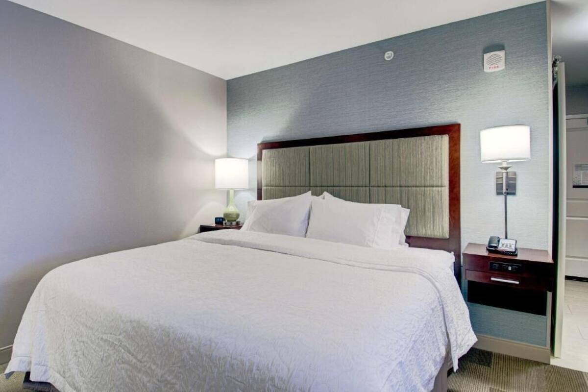 A hotel room with a large bed, two bedside tables with lamps, a wardrobe, and a small desk with a telephone.