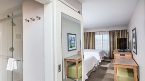 Une chambre d’hôtel avec une douche en verre, un lit, un bureau et une télévision.