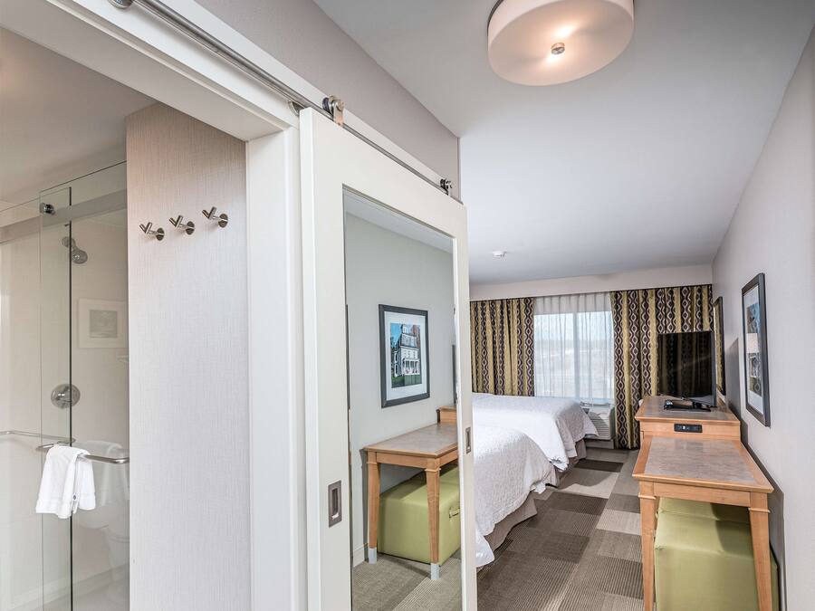 A hotel room with a glass shower, a bed, a desk, and a TV.