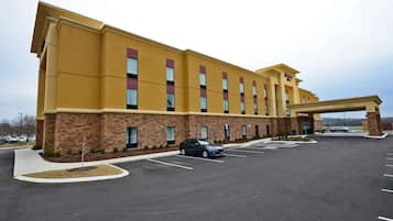 A hotel with a yellow facade, multiple windows, and a parking lot with a few cars.