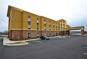 A hotel with a yellow facade, multiple windows, and a parking lot with a few cars.