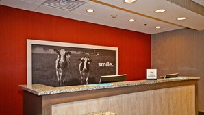 A hotel reception desk with a large poster of cows and the word "smile." on the wall. - Hampton Inn Pulaski (Pulaski)