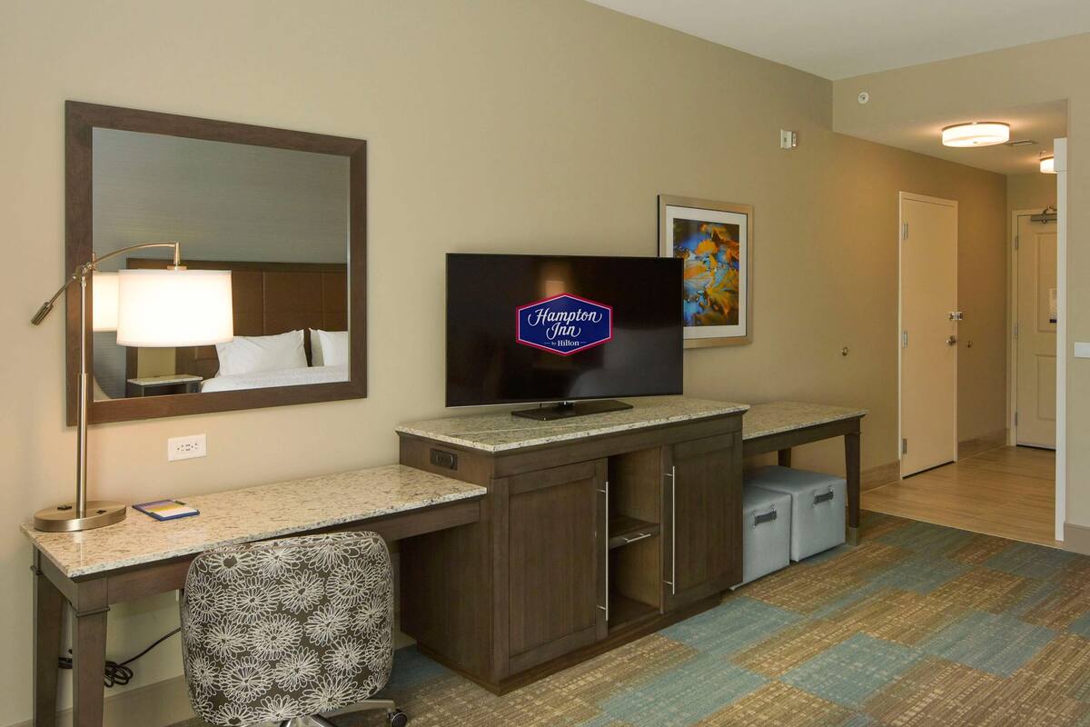 A hotel room with a desk, chair, television, and a carpeted floor.