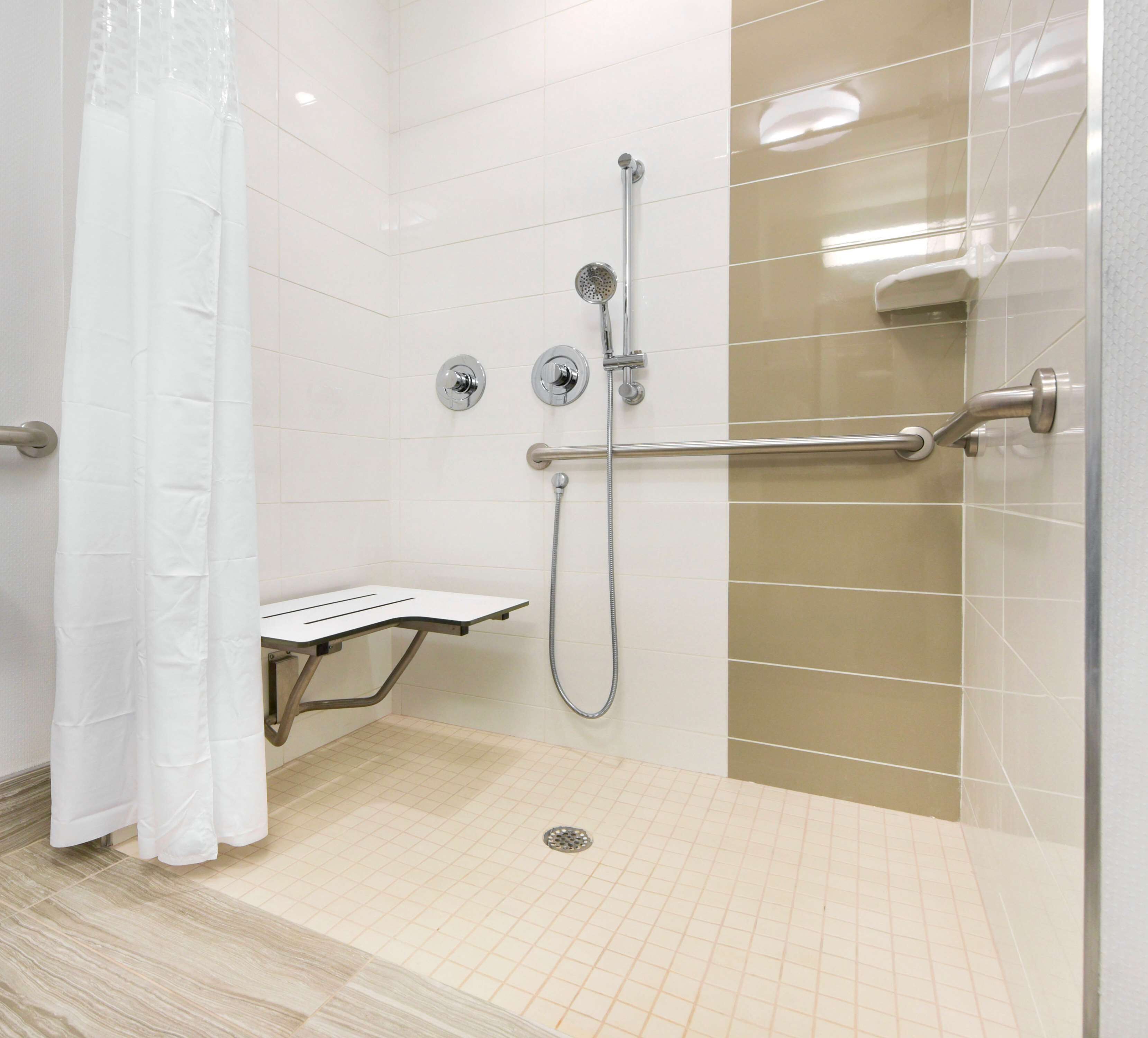 A walk-in shower with a grab bar, a white shower bench, and a showerhead.