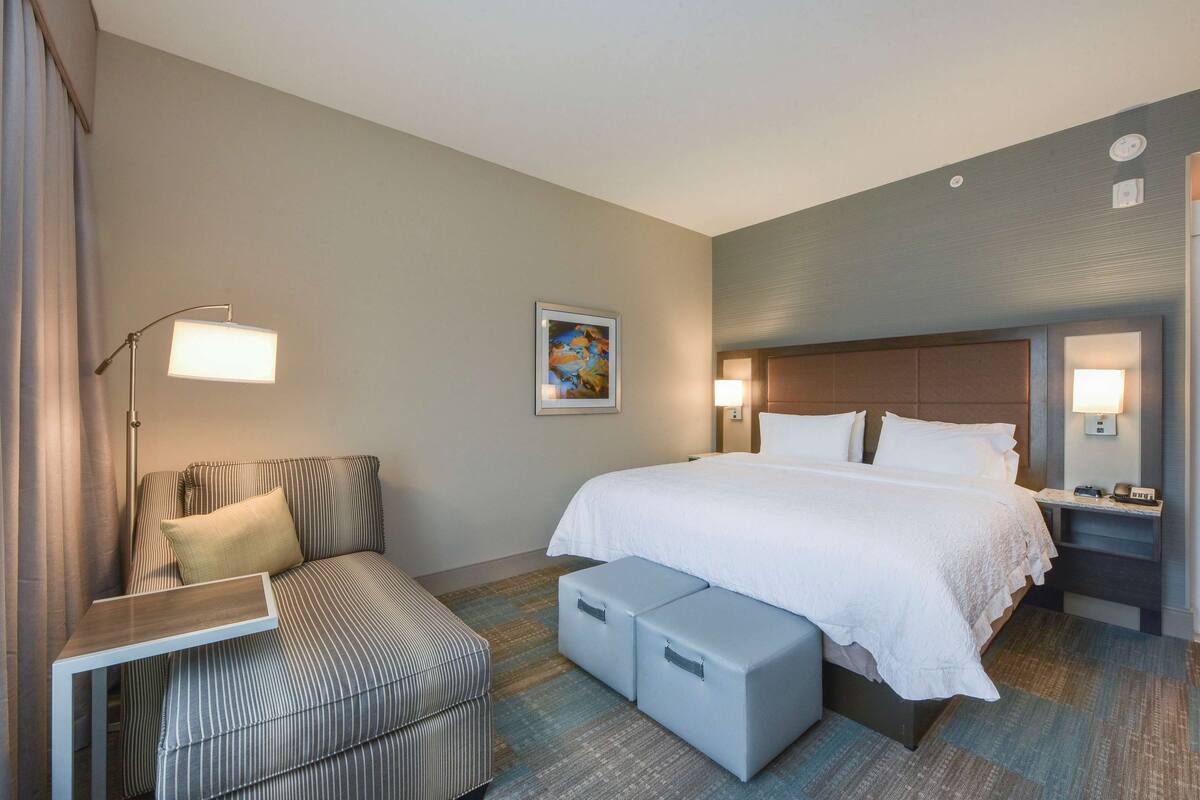 A hotel room with a bed, a sofa, a desk, and a nightstand with a lamp.