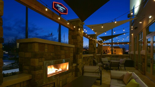An outdoor patio area with a stone fireplace, seating, and string lights. - Hampton Inn Lumberton (Lumberton)