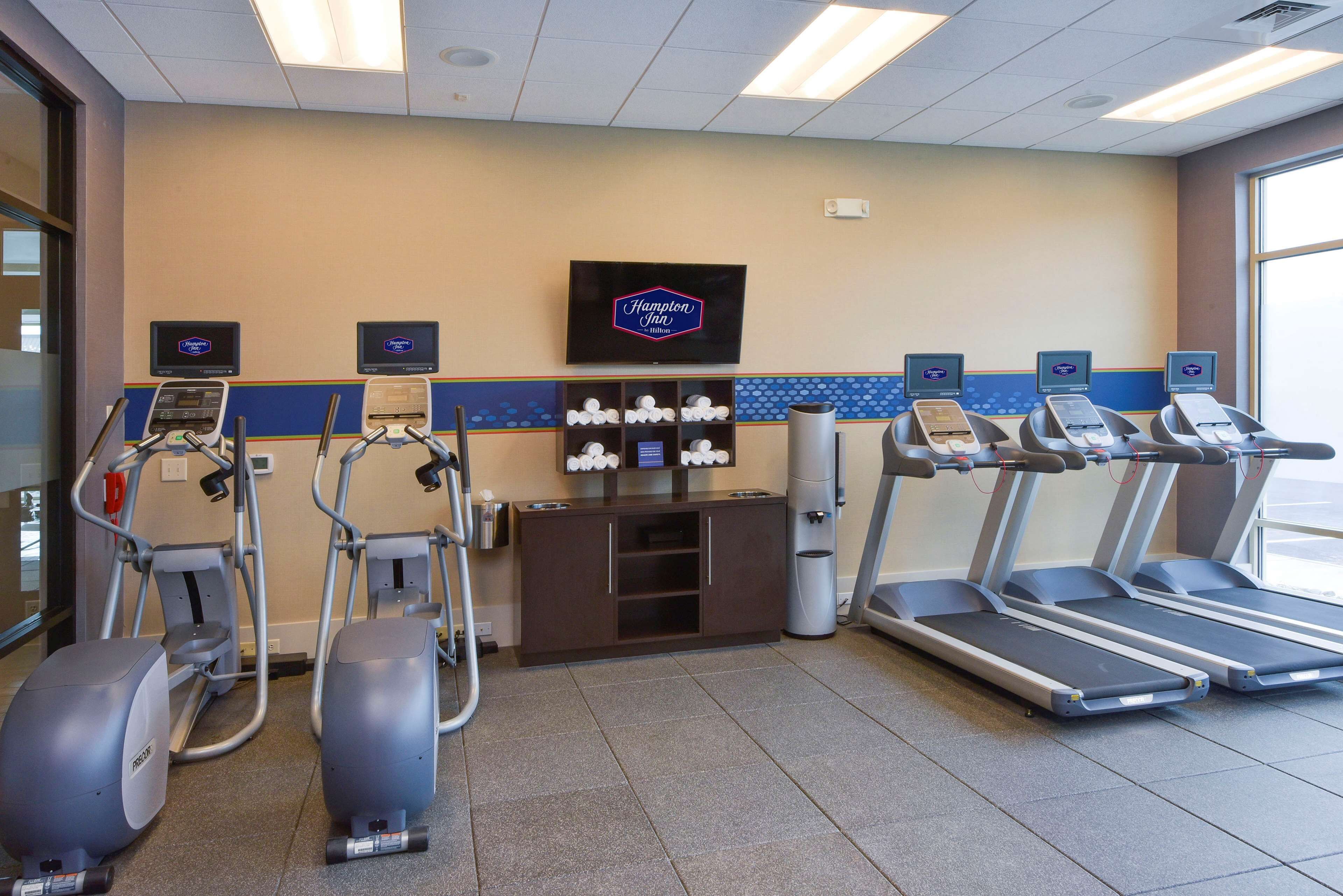 Ein Fitnessraum im Hotel mit Laufbändern, Crosstrainern und einem Fernseher, der den Namen des Hotels zeigt.