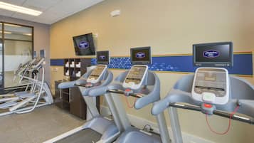 Un gimnasio con cintas de correr, bicicletas estáticas y una pantalla de televisión que muestra Hampton Inn.
