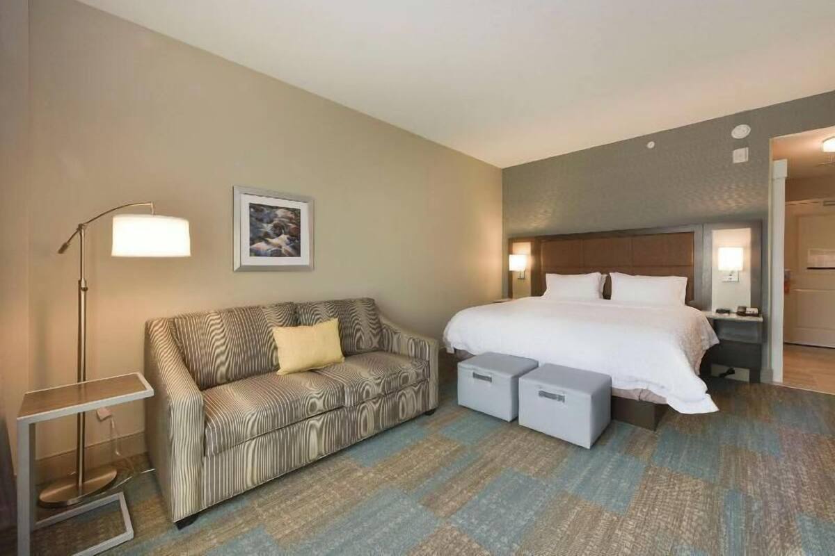A hotel room with a bed, a sofa, a side table, a lamp, and a framed picture on the wall.