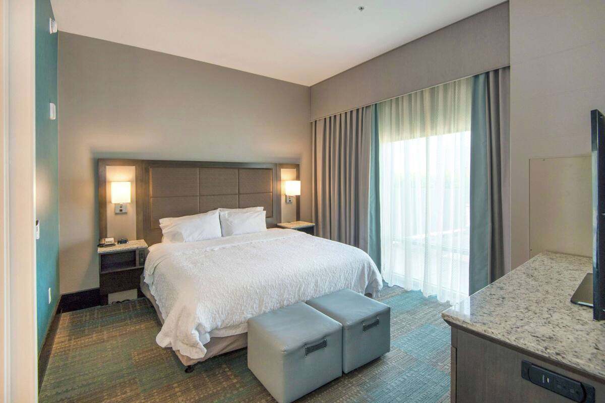 A hotel room with a large bed, a nightstand, a desk, a television, and a window with curtains.
