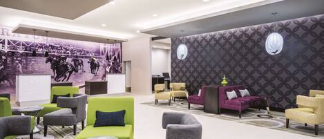 A modern lobby with green and grey seating, a patterned wall, and a mural of a horse race.