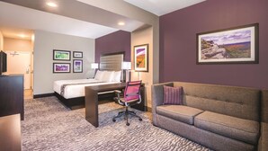 Een hotelkamer met een bed, bureau, stoel, bank en ingelijste foto's aan de muur.