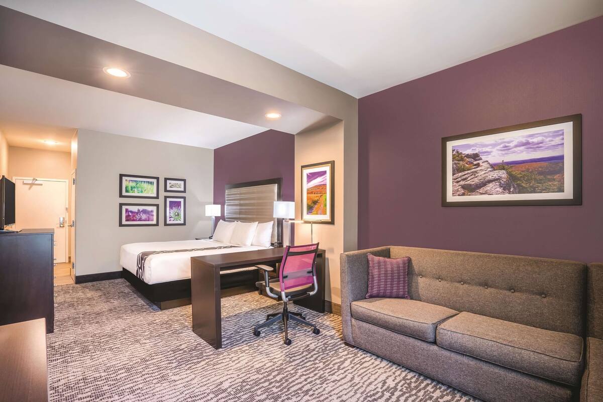 Een hotelkamer met een bed, bureau, stoel, bank en ingelijste foto's aan de muur.