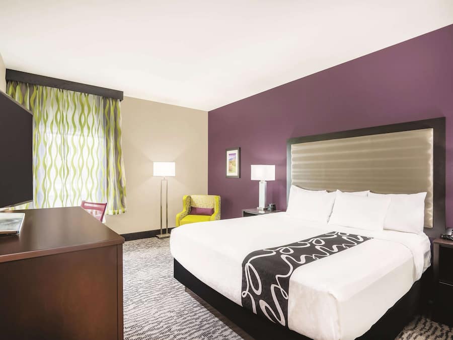A hotel room with a large bed, a desk, a chair, a TV, and a nightstand with a phone.